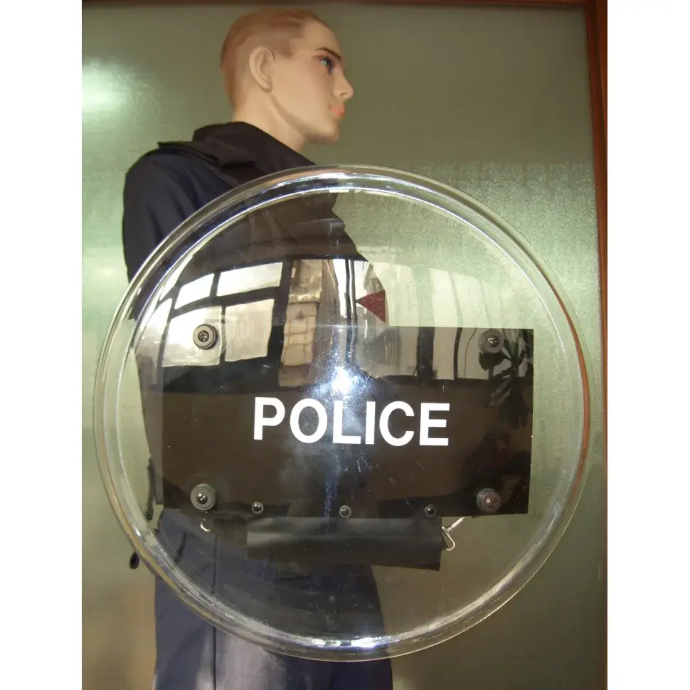 A mannequin wearing a ballistic vest is shown holding a round riot shield from the front, demonstrating protective equipment for riot control.